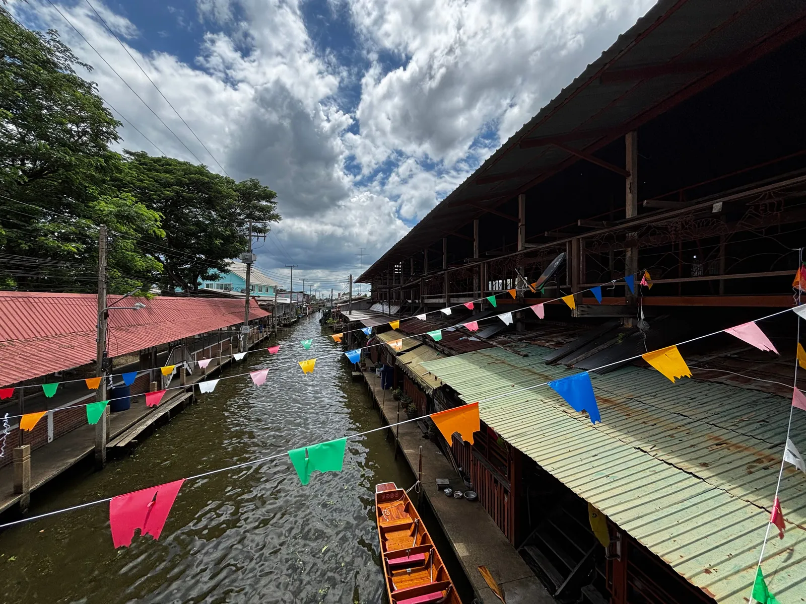 Wooden boats selling grilled seafood along a narrow canal lined with old shophouses at Amphawa Floating Market, Thailand