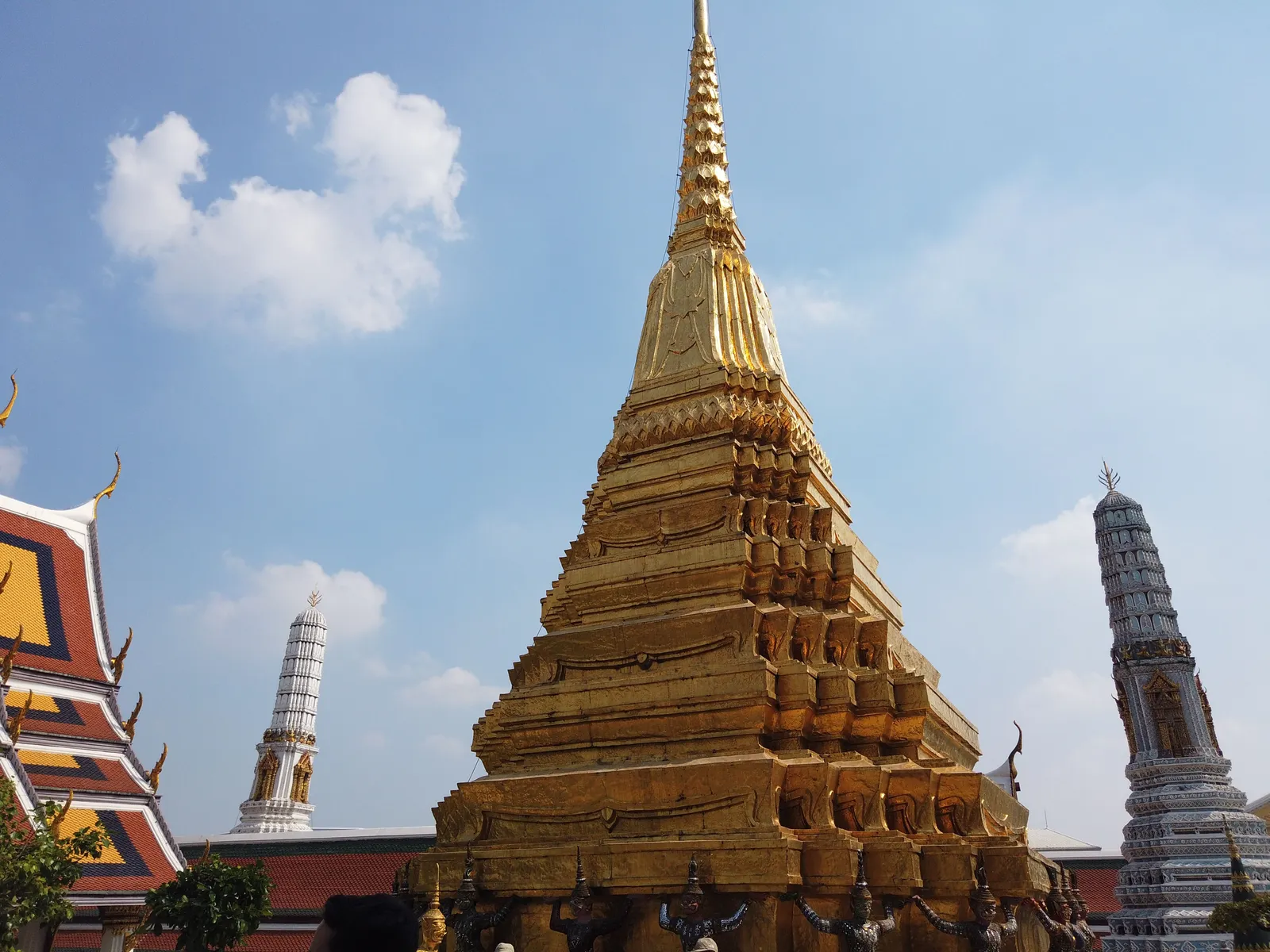 A golden chedi beside ornate temple spires under a blue sky