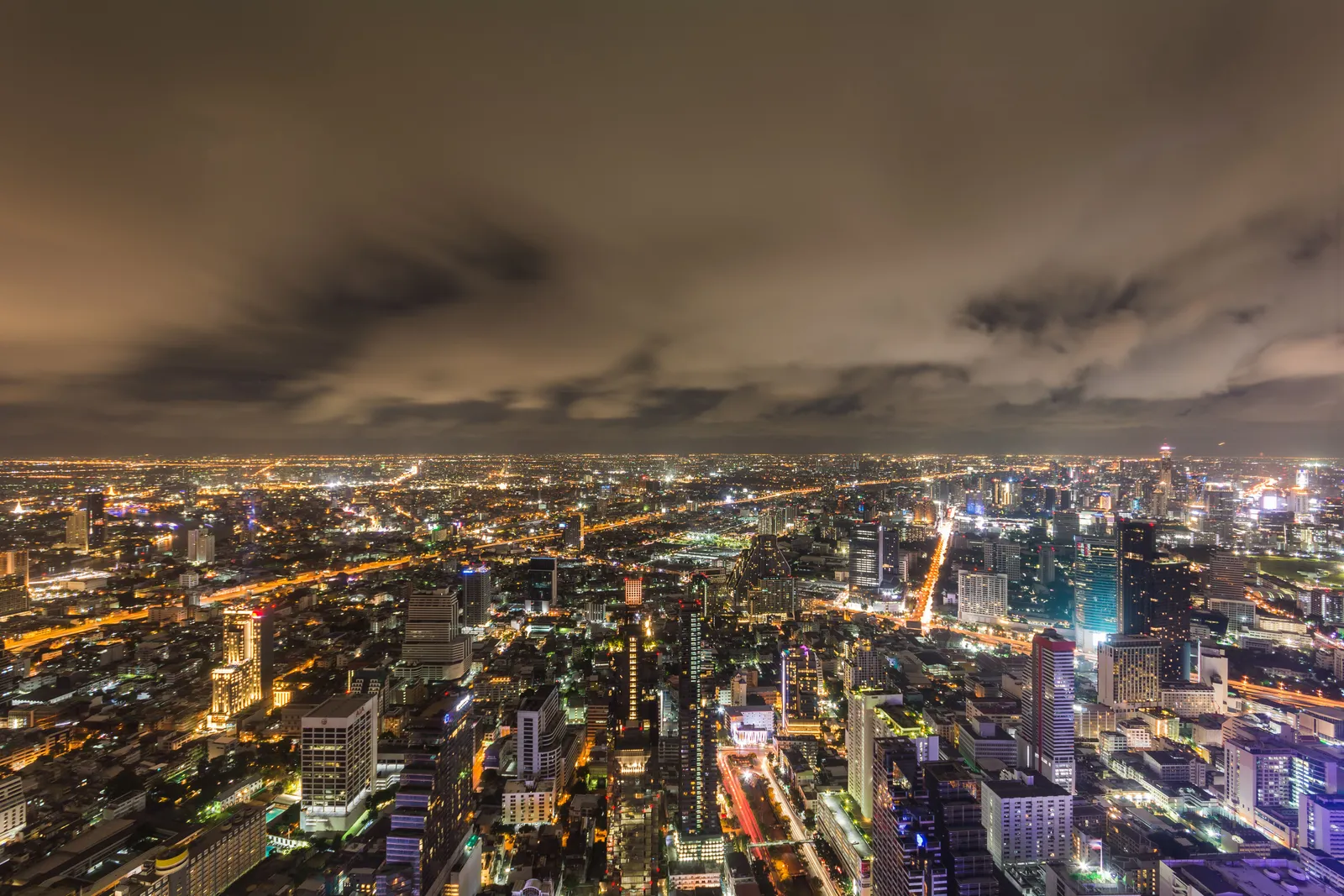 The illuminated Bangkok skyline seen from a high-rise rooftop bar terrace at night