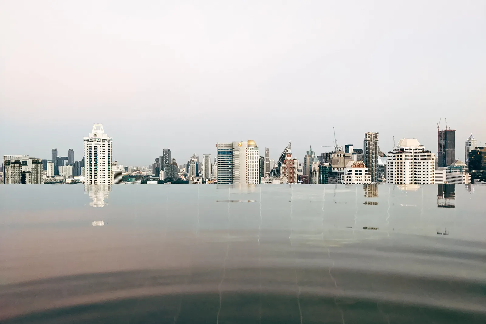 The Bangkok skyline seen across the still water of a rooftop pool at dusk, Thailand