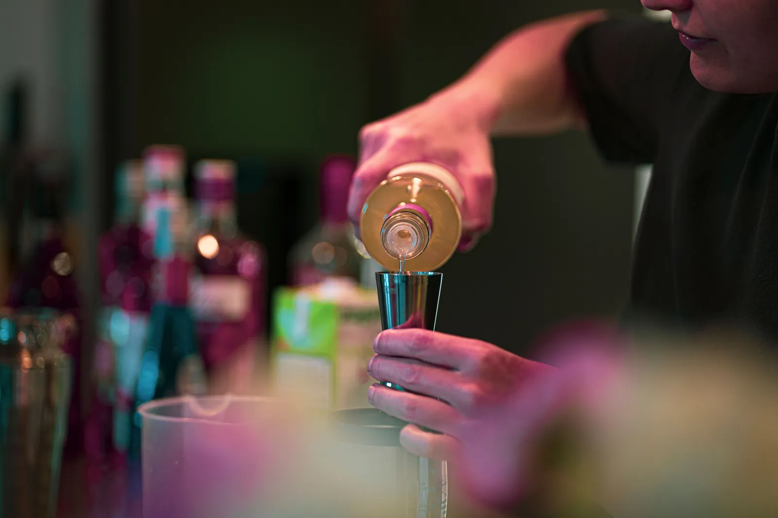 A bartender pouring a cocktail behind a dimly lit bar counter