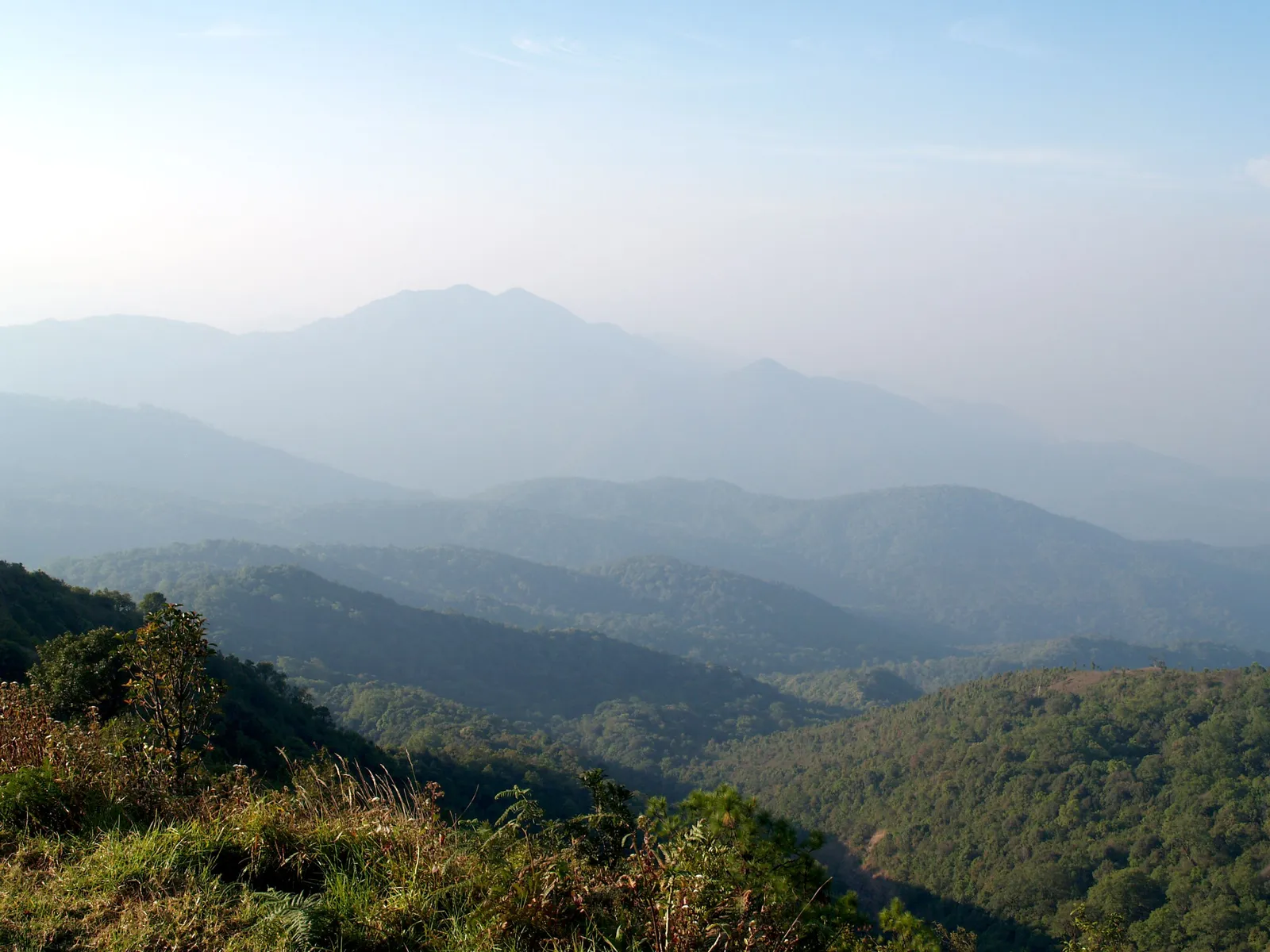 Forested mountain ridges near Chiang Mai, Thailand, fading into thick haze under a pale sky