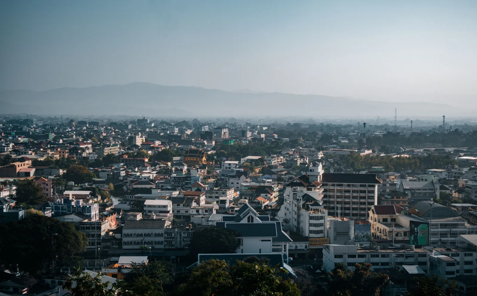 The rooftops of Chiang Mai, Thailand, under flat grey haze during the northern smoke season, with the hills barely visible behind