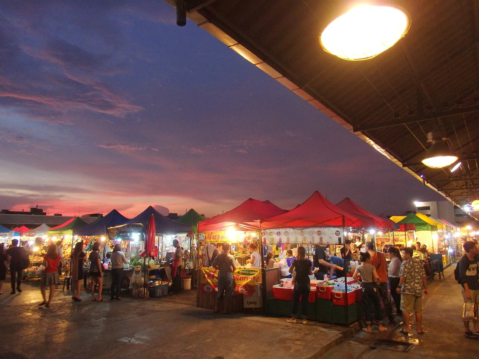 A busy Bangkok street lined with food stalls and tuk-tuks under warm evening light in Thailand