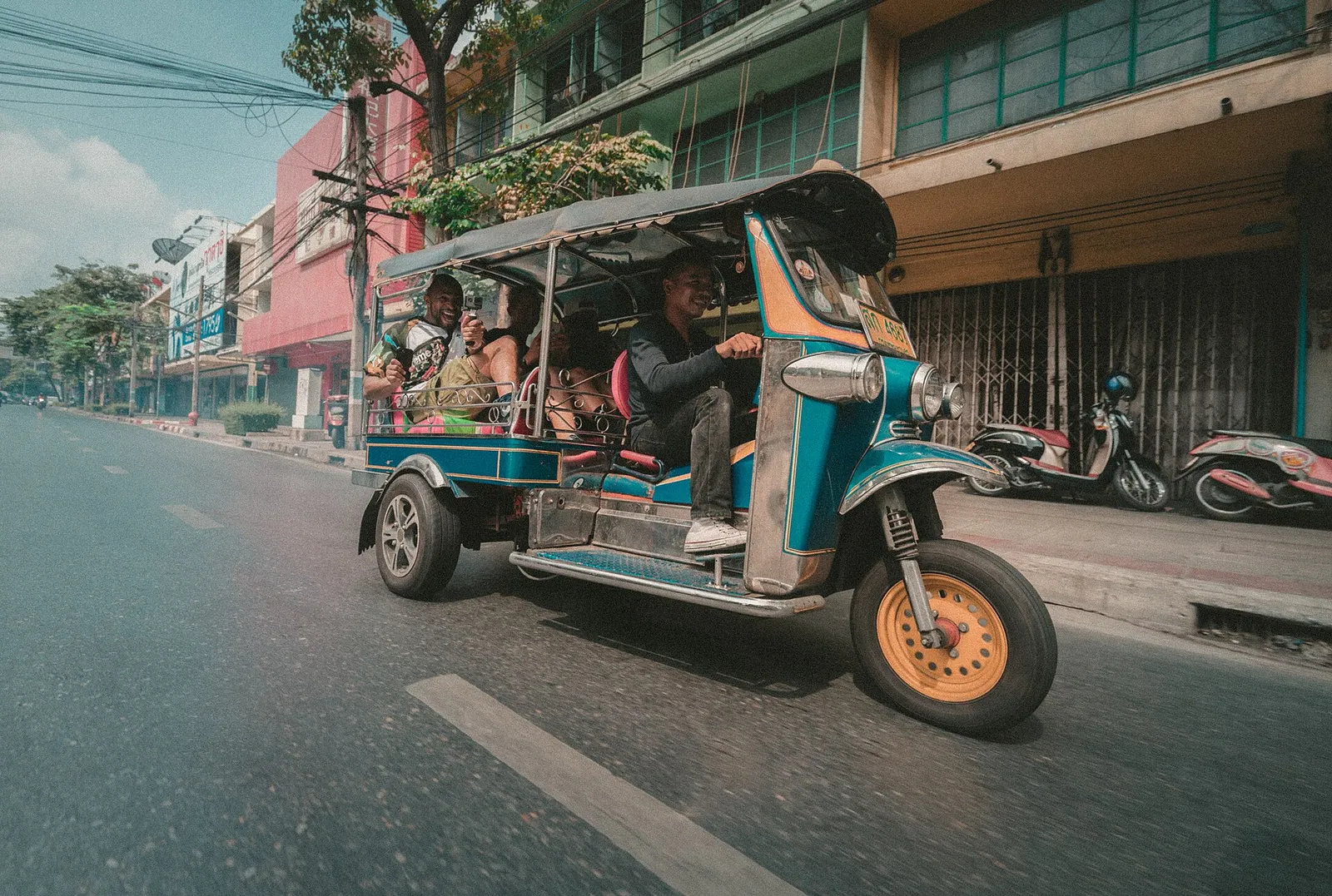 A row of scooters and a tuk-tuk parked on a quiet street in a northern Thai town