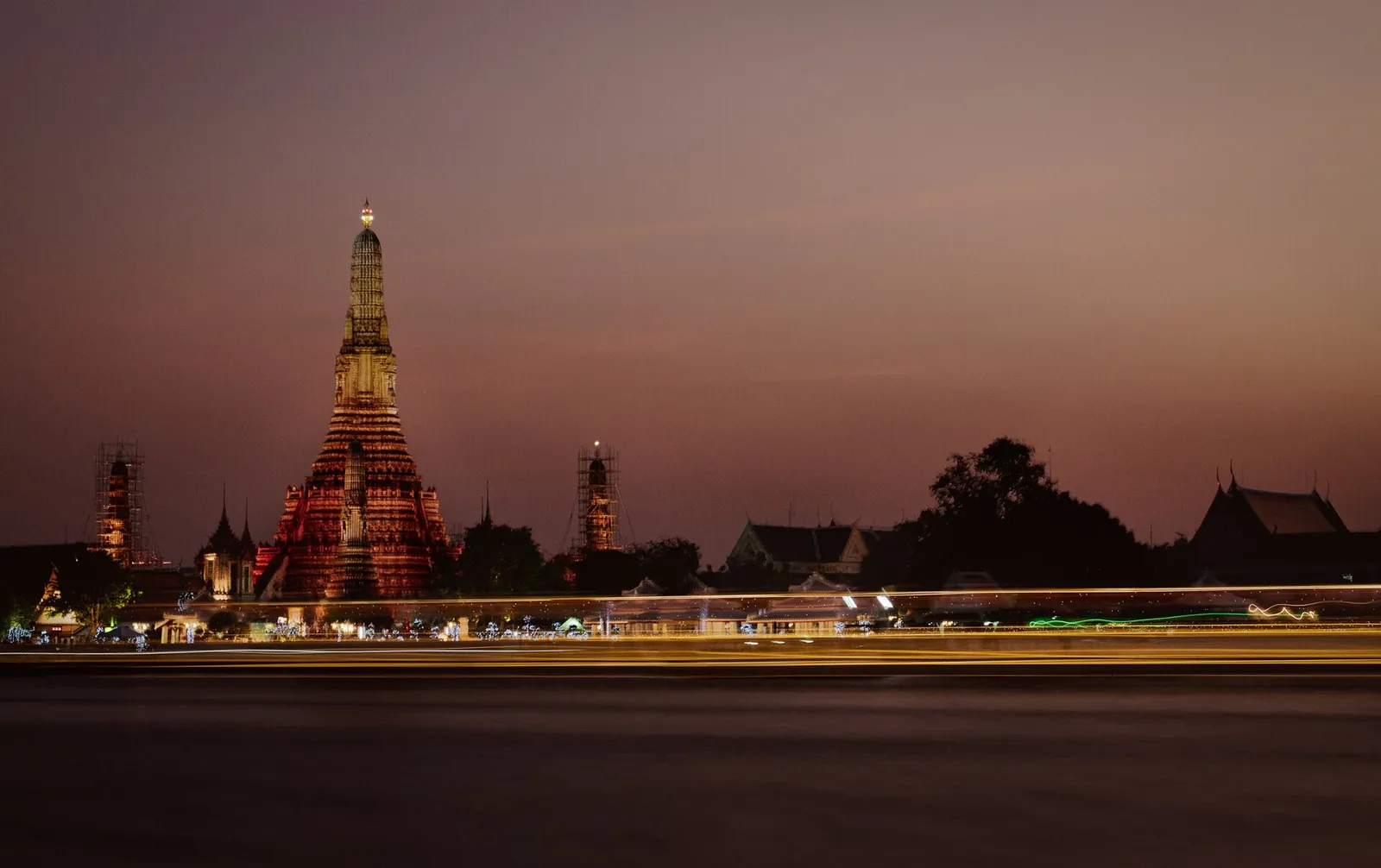 Wat Arun temple spire glowing at dusk beside the Chao Phraya river in Bangkok