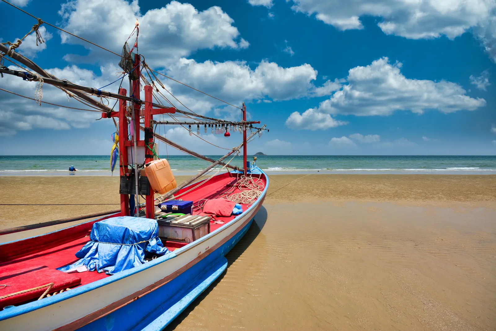 A long sandy beach at Hua Hin with fishing boats pulled up on the sand and a calm sea, Thailand