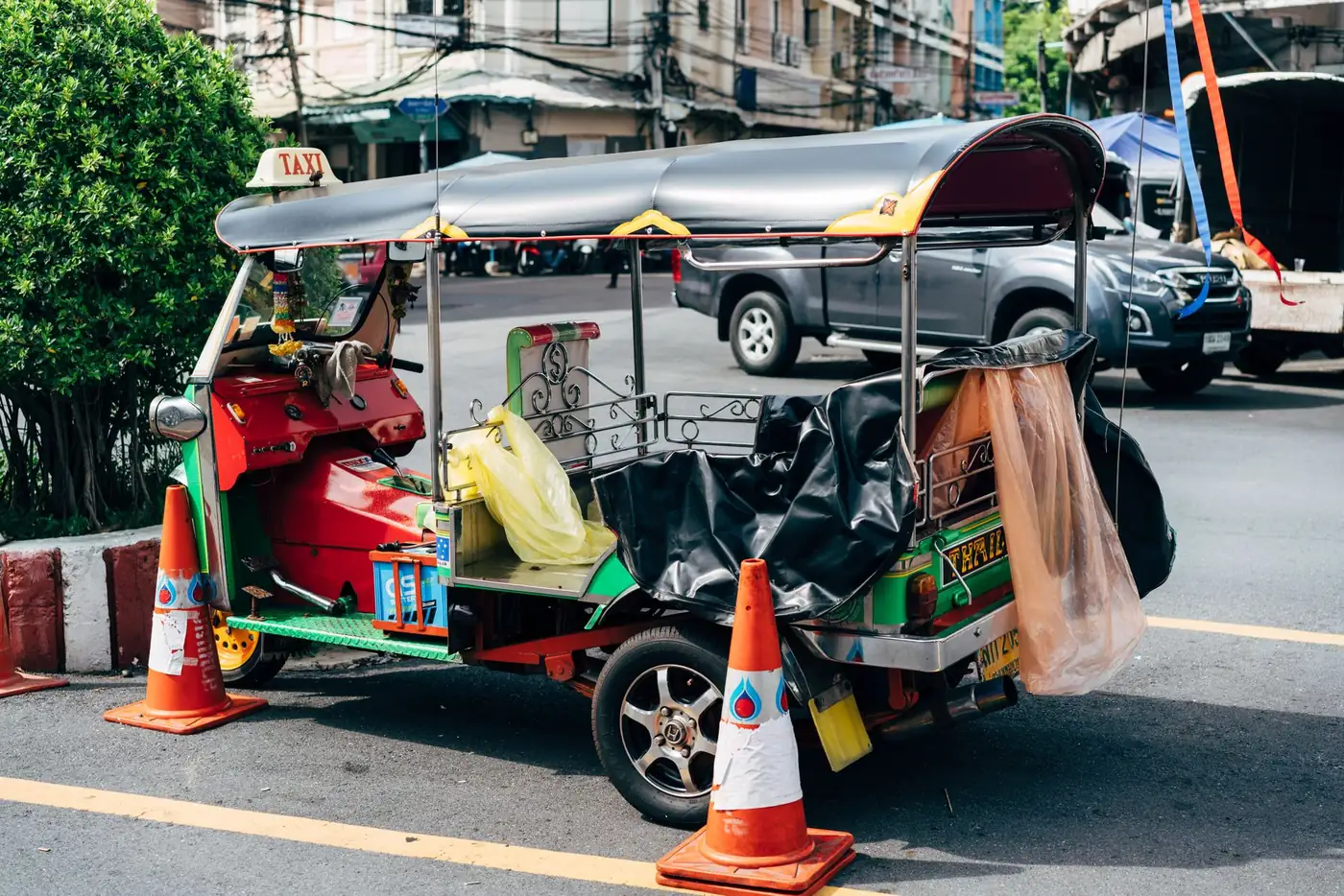 A tuk tuk taxi parked beside traffic cones on a busy street in Bangkok, Thailand