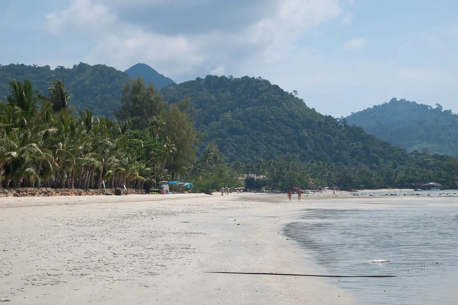 A quiet sandy beach with palm trees and forested mountain peaks behind it on Koh Chang, Thailand