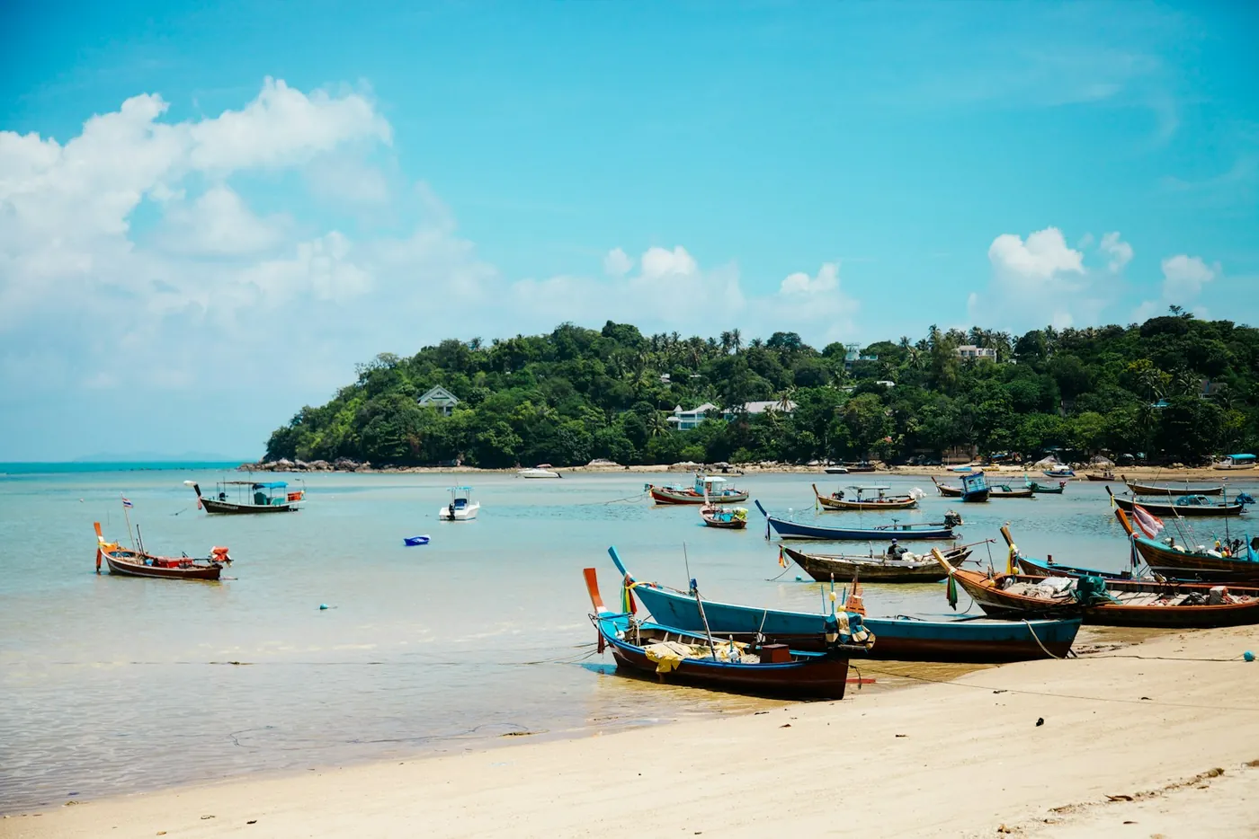 A long curving beach with boats and hills behind on Koh Samui, Thailand