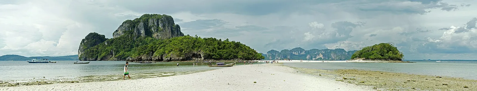 A longtail boat moored in shallow turquoise water below cliffs in Krabi, Thailand