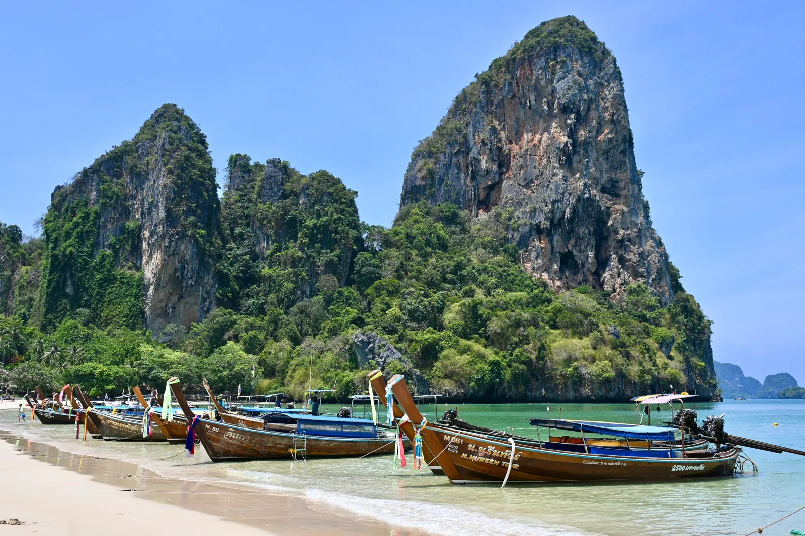 Longtail boats moored on a beach beneath towering limestone cliffs in Krabi, Thailand