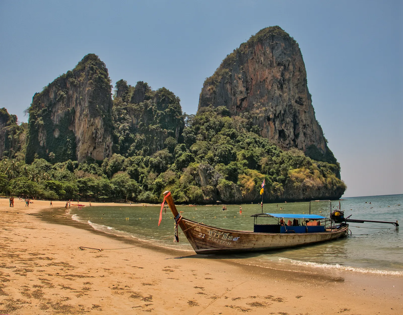 A longtail boat approaching a beach backed by sheer limestone cliffs at Railay, Thailand