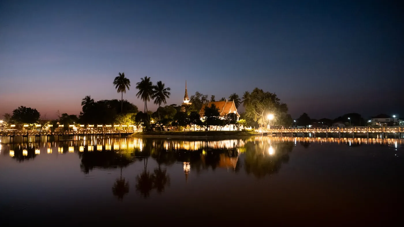 A lit temple reflected in still water at dusk in Sukhothai, Thailand