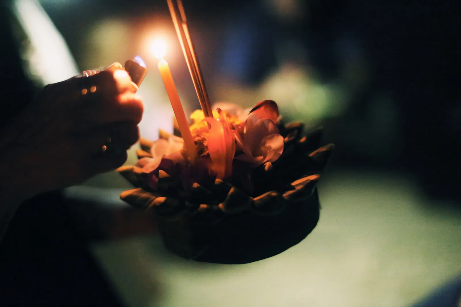 A hand lighting the candle on a decorated krathong float at night
