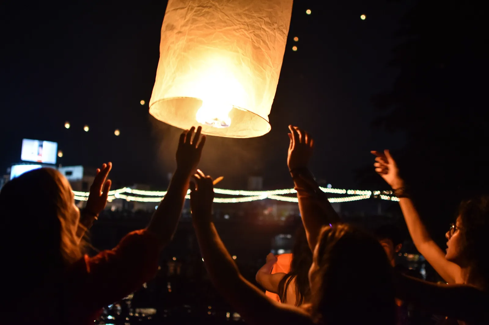 A glowing paper sky lantern being released into the night sky by raised hands during Yi Peng