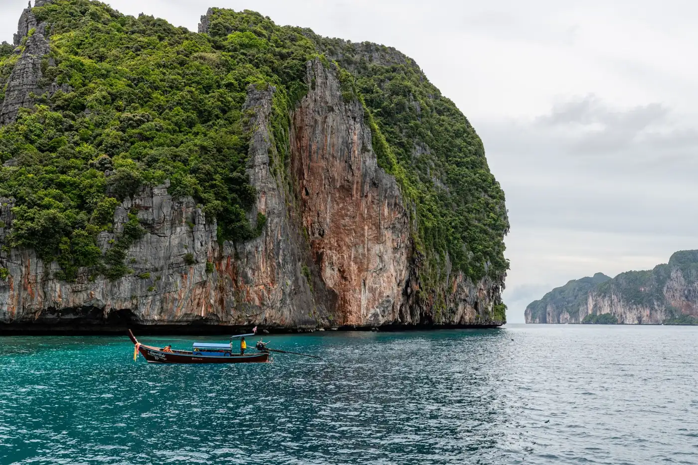 Limestone cliffs rising from turquoise water with a traditional longtail boat, a common sight along Thailand's karst coastline