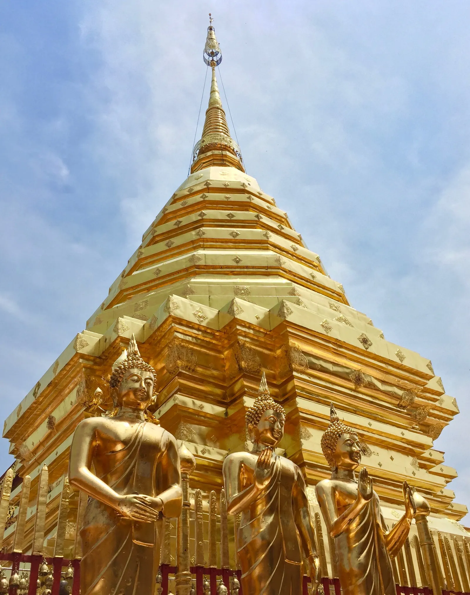 The golden chedi of Wat Phra That Doi Suthep in Chiang Mai, northern Thailand, with gilded Buddha statues standing at its base under a clear blue sky