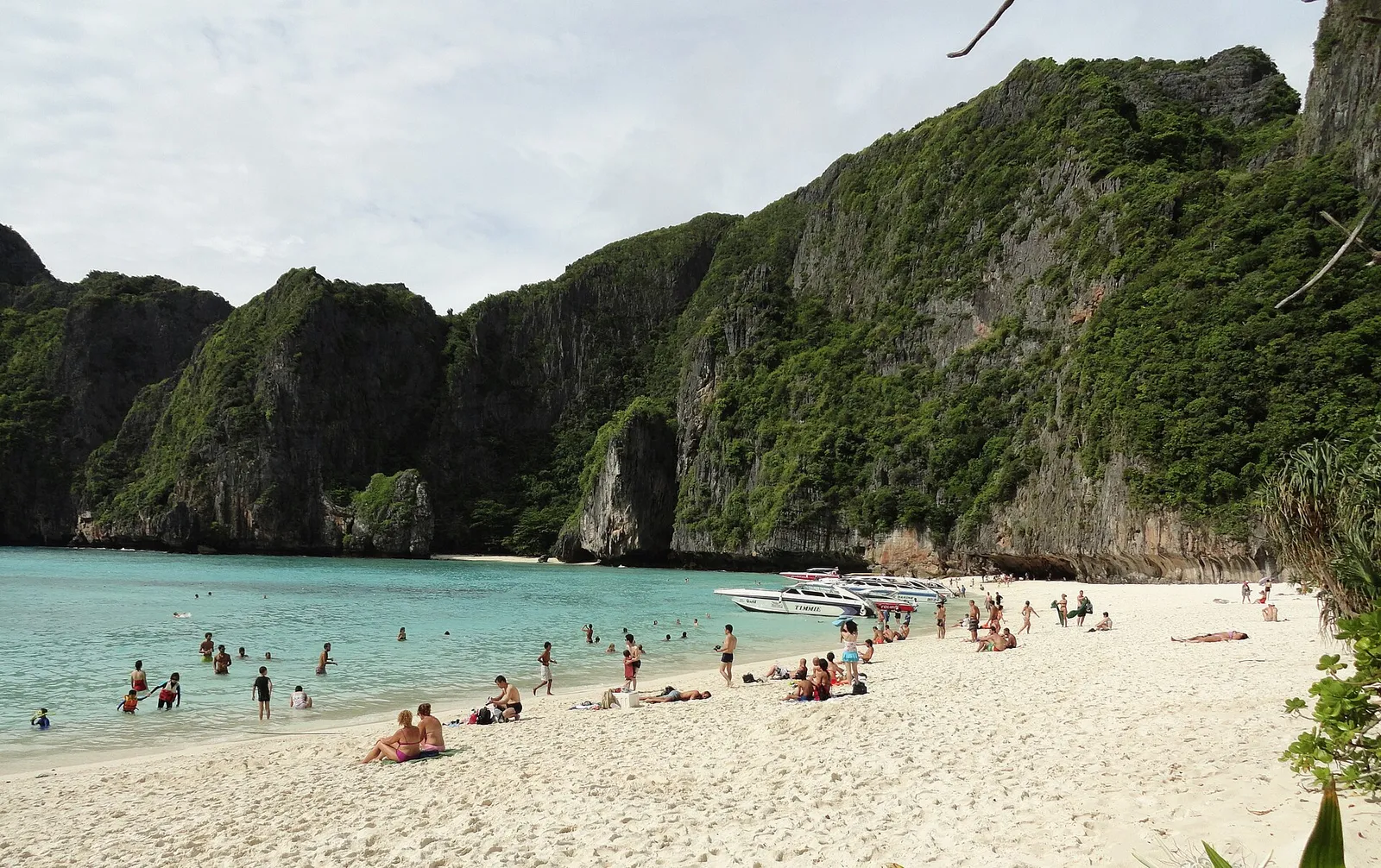 A white sand beach ringed by limestone cliffs at Maya Bay on Phi Phi Leh in southern Thailand, with turquoise water and tour boats moored offshore