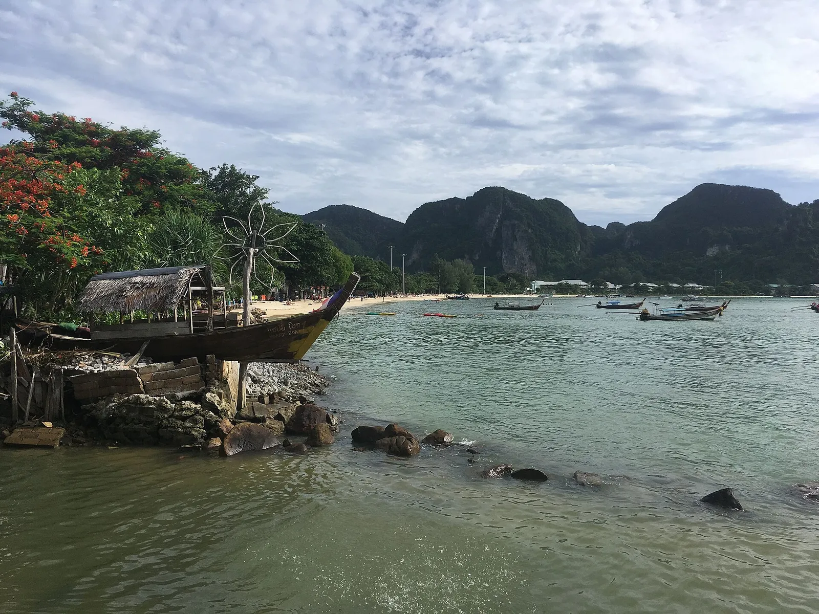 A longtail boat drawn up on a beach below limestone cliffs at Phi Phi, Thailand