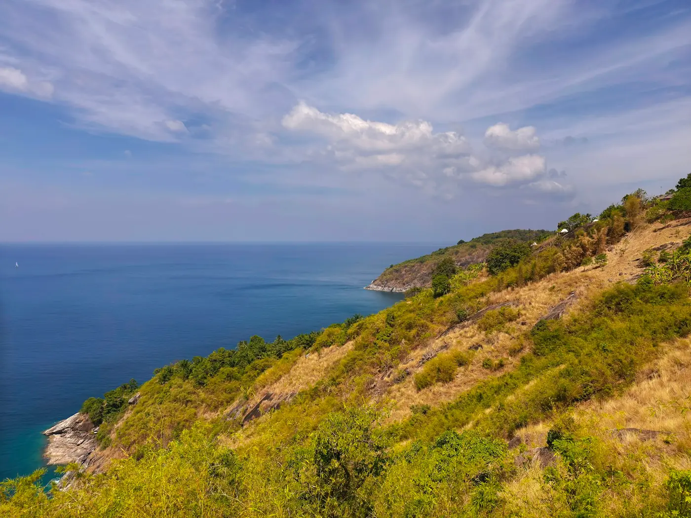 A green headland above a curving bay on the coast of Phuket, Thailand