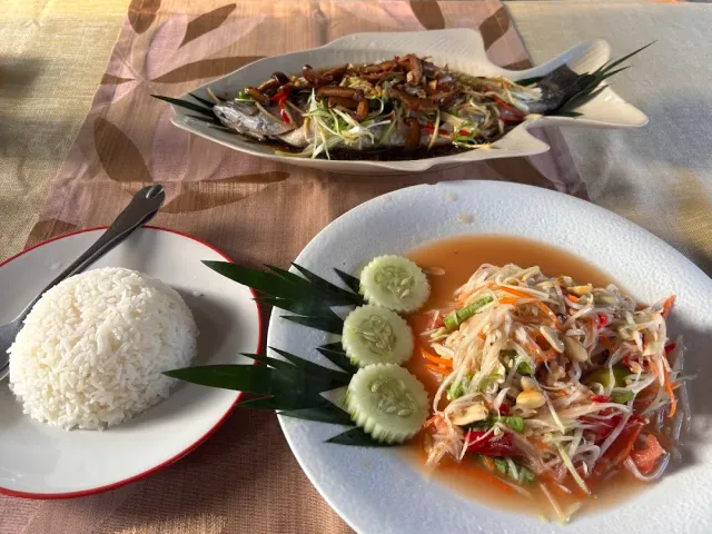 A plate of whole fish, papaya salad with cucumber and a plate of white rice