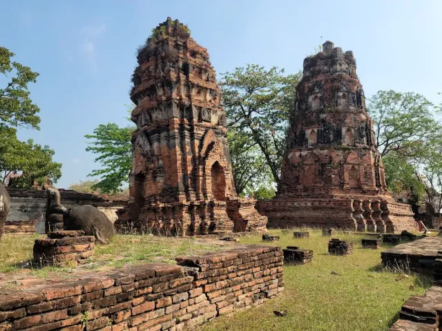 Two crumbling red brick towers among low ruined walls and grass