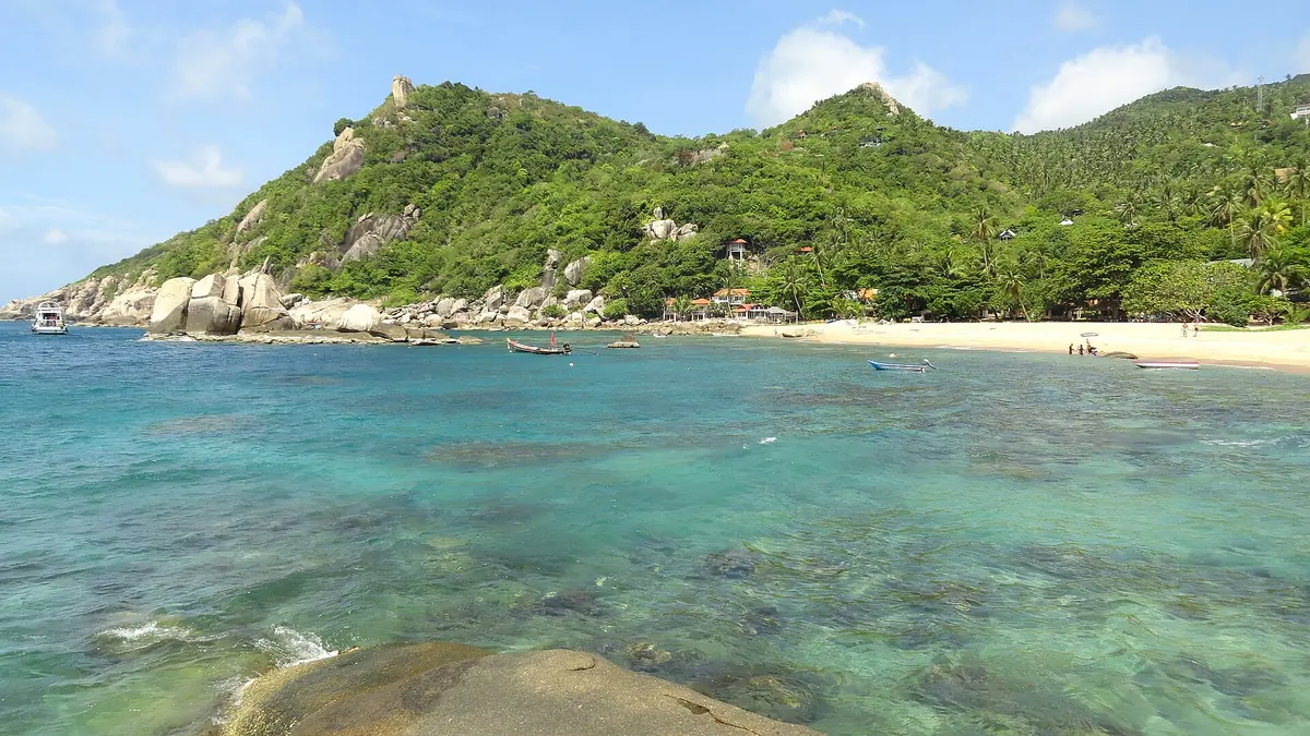 Tanote Bay on Koh Tao, shallow turquoise water over the reef, a strip of sand and granite boulders on a wooded headland