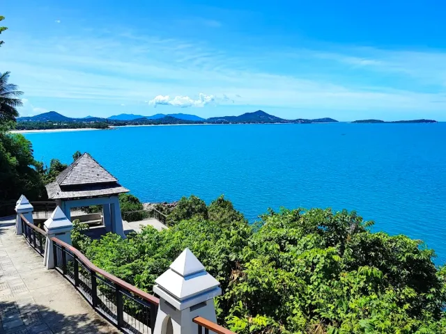 A tiled roof pavilion on a green slope facing a wide blue bay