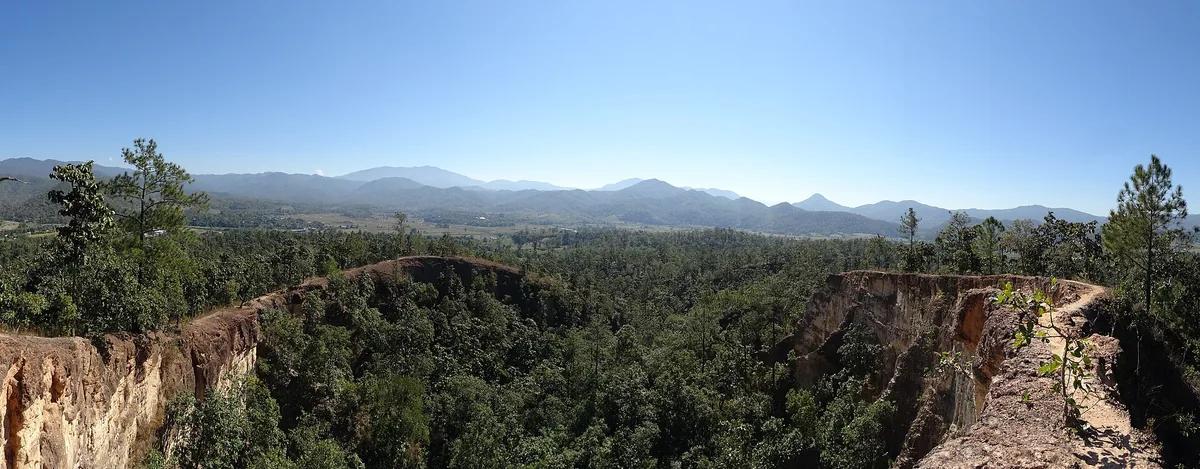 Narrow red earth ridges covered in green vegetation above a valley, with blue hills on the horizon
