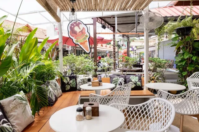 An open seating corner with white metal chairs, leaf print cushions and greenery around