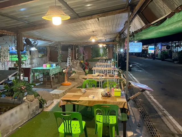 Tables with green tablecloths and green plastic chairs under a lit canopy in the evening