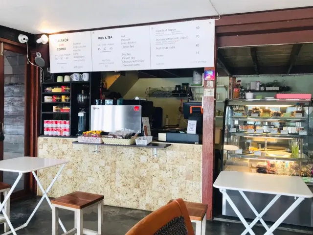 An order counter with hanging menus, an espresso machine and a lit dessert display beside tables