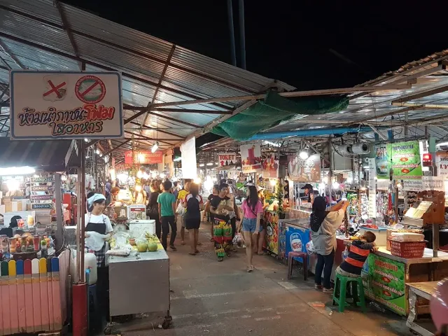 A covered aisle between food and goods stalls, shoppers walking about in the evening
