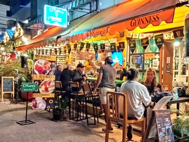 An orange awning and lit menu signs, diners sitting at outdoor tables at night