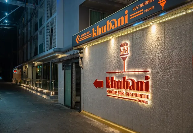 A white entrance wall with an orange lit sign and an arrow directing visitors in the evening