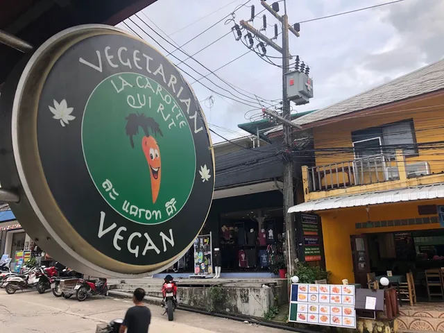 A round sign with a cartoon carrot above a street with motorbikes and shops
