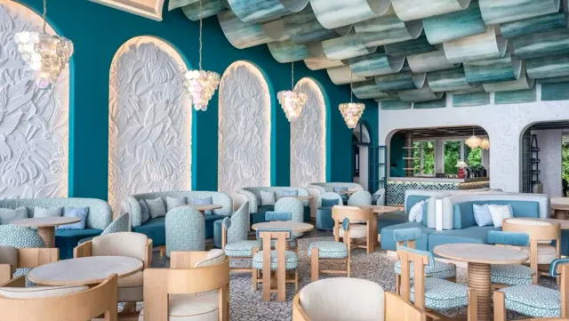 A turquoise toned space with carved plaster arches, shell chandeliers and designer armchairs