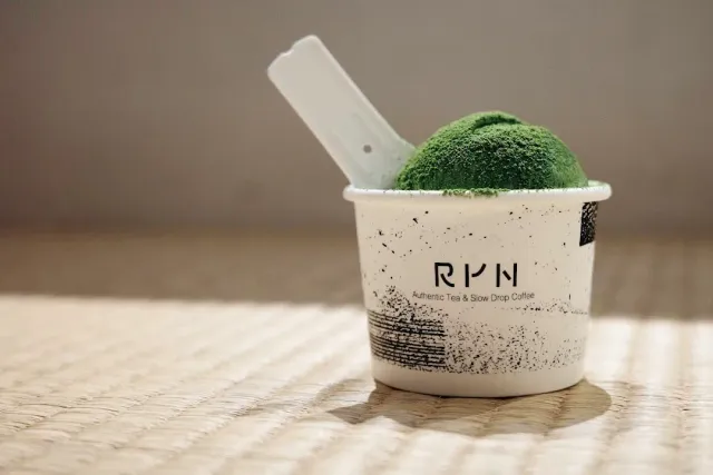 A paper cup with a scoop of green ice cream and a spoon, on a light straw mat