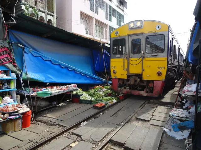 A yellow train passing between market stalls and fabric awnings on both sides of the track