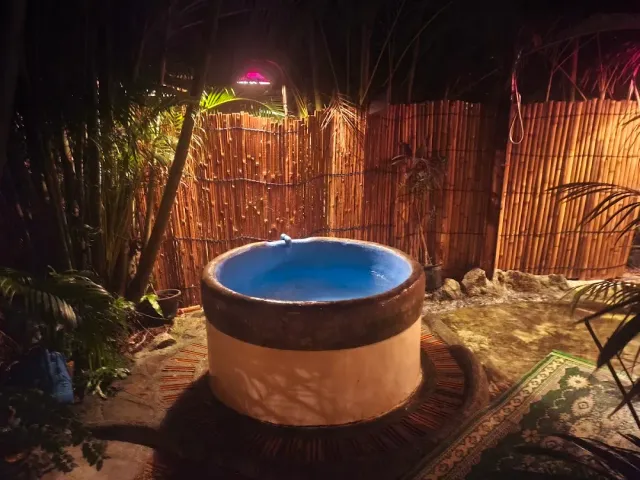 A round plunge tub with blue water at night, a bamboo fence and greenery around