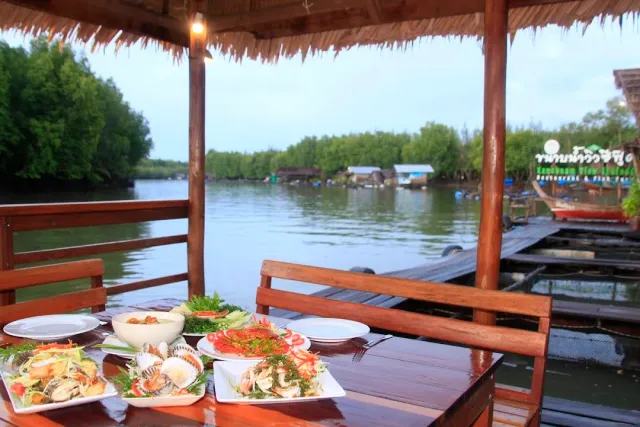 A wooden hut above the water with plates of crab and shellfish and long boats in the background