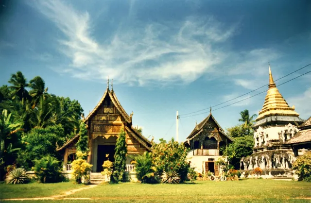 A Lanna style temple hall with tiered wooden roofs and a gilded chedi behind it