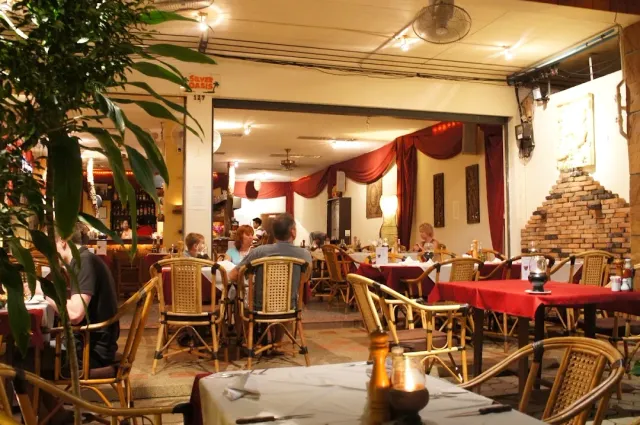 A hall at night with rattan chairs, red tablecloths and an arched brick wall