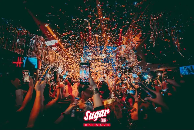 A crowd with raised phones on a club dance floor, under a shower of golden confetti