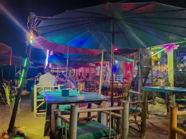 A beach bar at night with large parasols, bamboo furniture and colorful neon lighting