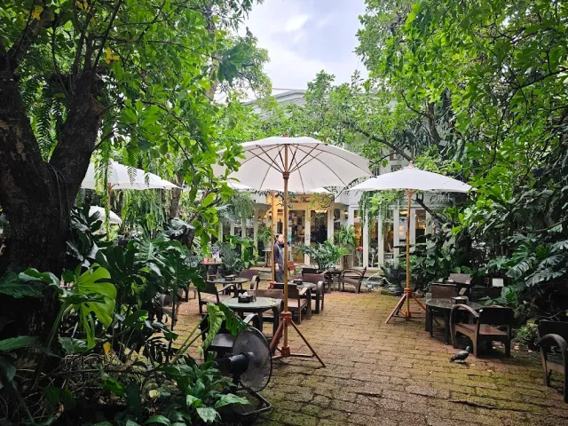 A garden dense with trees, white parasols, outdoor tables and a stone path