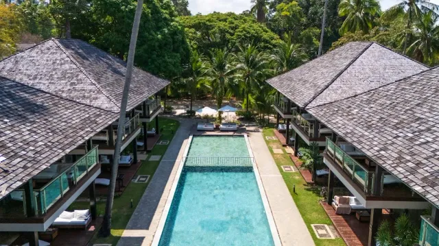An overhead view of a long pool between two shingle roofed buildings, and palms