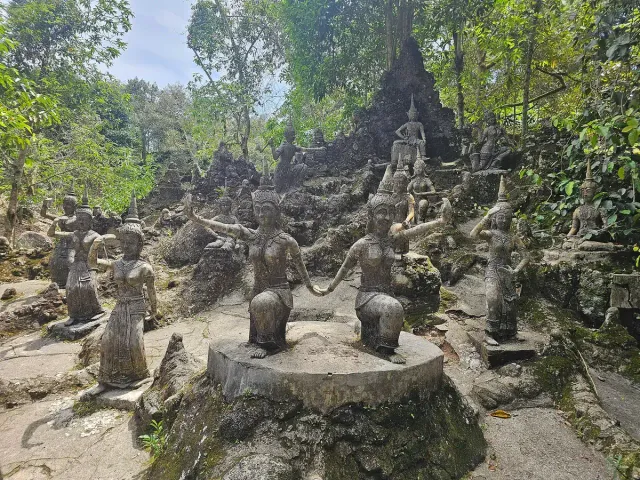 Dozens of stone figures scattered across a green jungle slope around stone steps