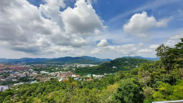A hilltop view over town roofs and green hills under white clouds